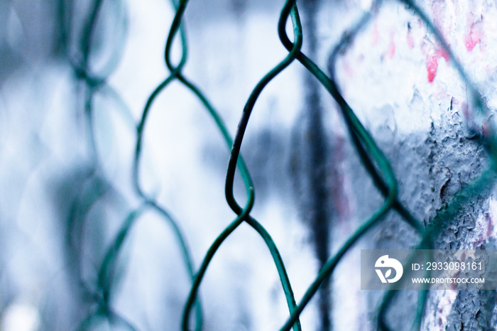 Metal anti-advertising grid on the transformer panel close-up. Abstract background with a dark green wire fence against a blue sky.