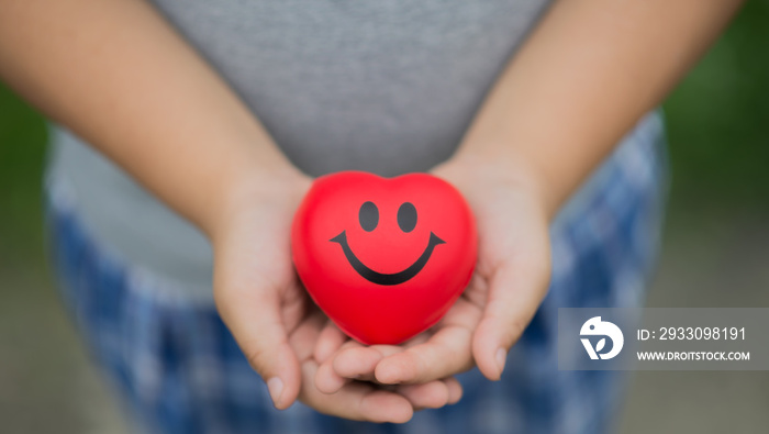 Attractive Asian boy holding a red heart with a smile. On both palms The concept of important dates Such as Cancer Day, World Heart Day, Happy Savings Day