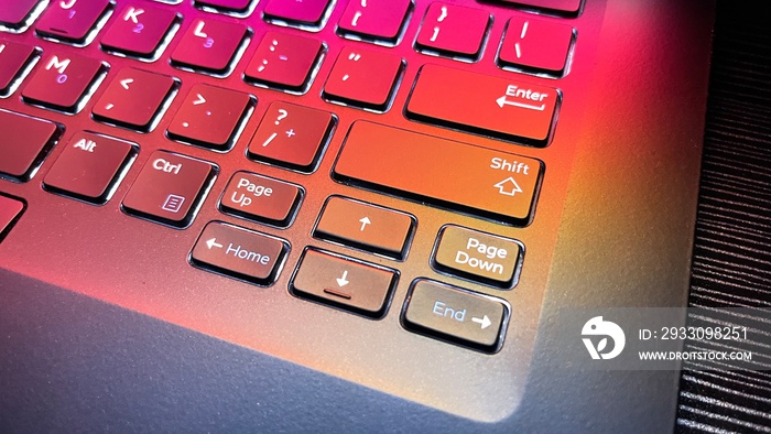 Studio shot of closeup of laptop keyboard illumination, backlit keyboard lit with colorful desktop screen wallpaper in a dark room