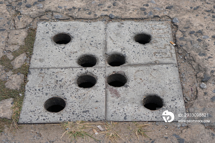 Balcony steel drain hole mesh and green leaves. Black metal Drainage grate for draining, directing excess water down into the sewers and prevent flooding. Dandelions sprouted between the tiles