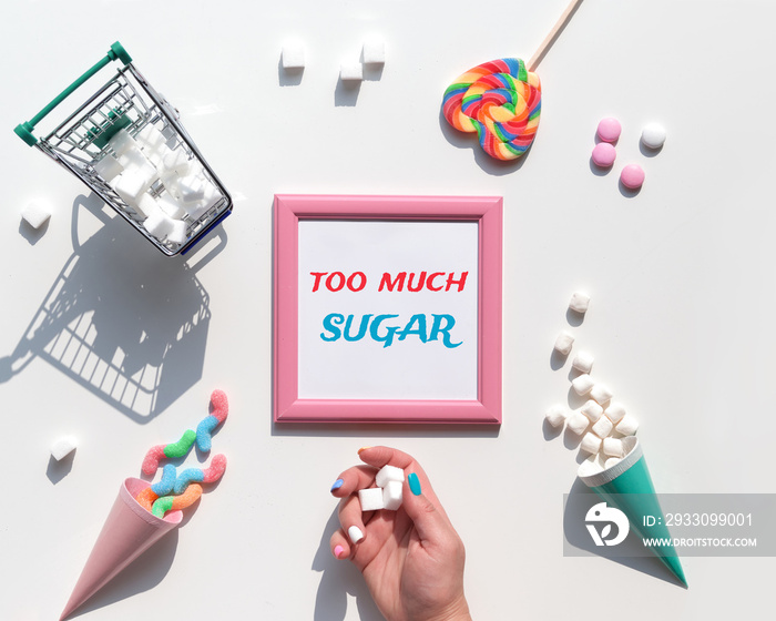 Text Too Much Sugar. Excess of sweets, chocolate, candy, sweet food in hand. Various tasty snacks in pastel colors, pink, mint green, on white background. Text in pink square frame. Sugar tax concept.