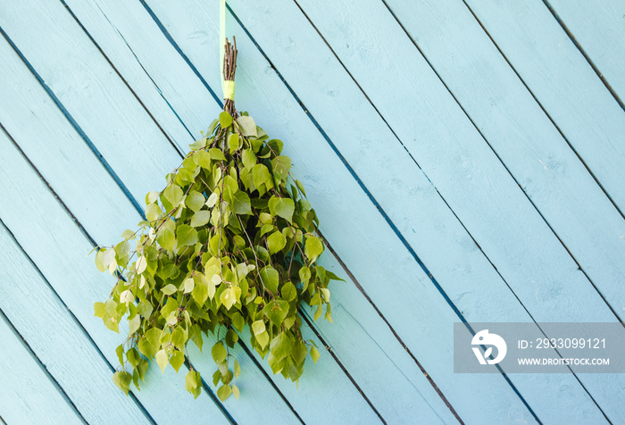 Birch tree sauna whisk broom ( also known as vasta, vihta or venik) hanging and drying on the wall, blue wooden background, copy space. Whisk is used in sauna to massage body and increase blood flow.