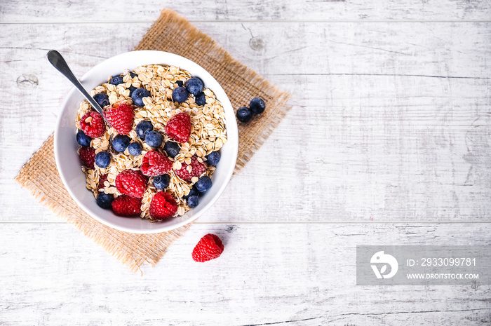 Top view of oat flakes with forest fruits. Raspberries and blueberries in white plate with oat flakes on jute.