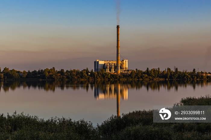 Old Garbage incineration plant on Lake bank. Old Waste incinerator plant with smoking smokestack. Colorful sky background