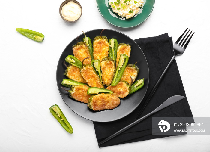 Plate with tasty jalapeno poppers and sauce on white background