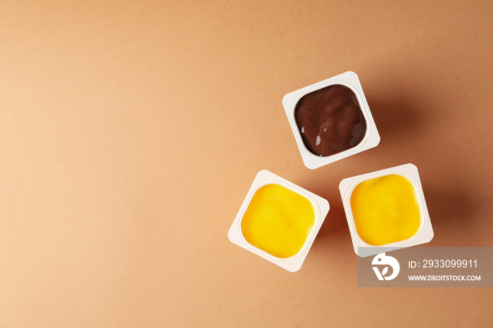 Plastics cups of yogurt on brown background, top view