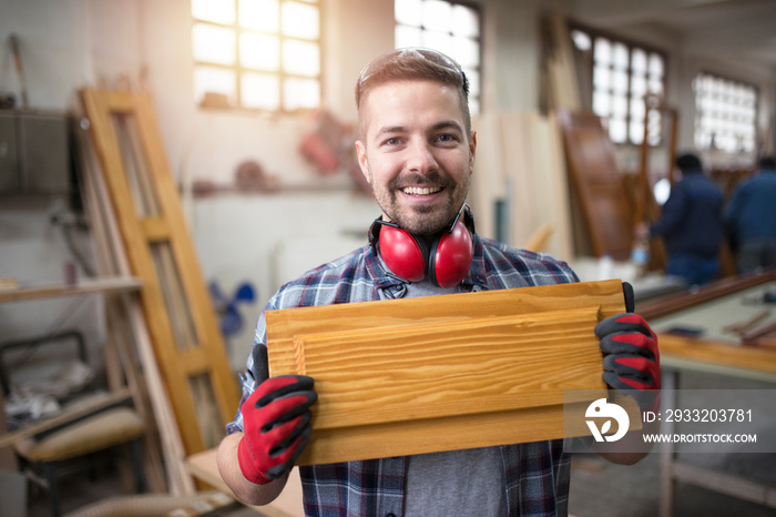 Portrait of smiling craftsman holding piece of furniture in his carpentry workshop. Creative carpent