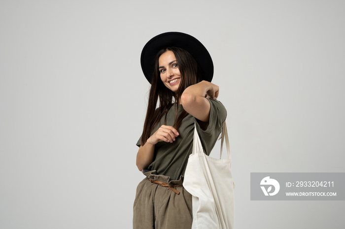 Happy smiling brunette woman in black hat with white cotton eco bag on her shoulder. Girl holding te