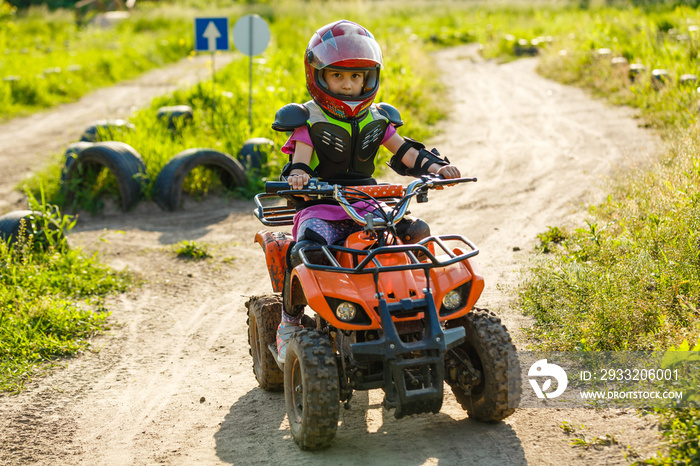 The little girl rides a quad bike. A mini quad bike is a cool girl in a helmet and protective clothi