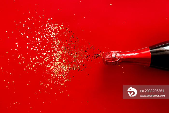 New Year background. Closed bottle of red champagne with golden sparkles on red background.