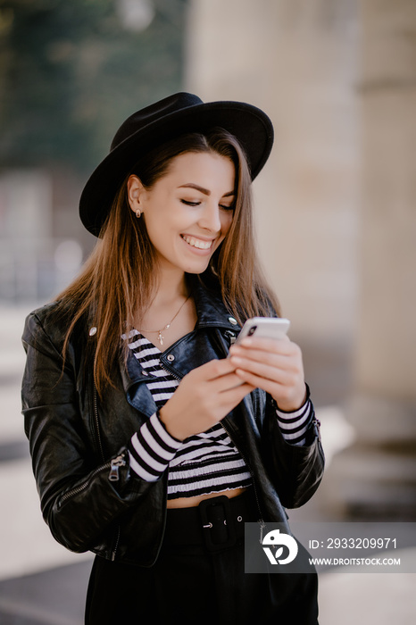 Young pretty Girl in hat and sunglasses checking her smart phone walking in the street outdoors