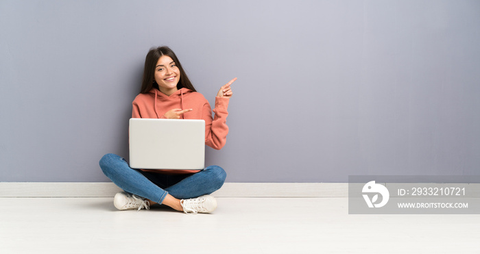 年轻的学生女孩，笔记本电脑放在地板上，手指指向侧面