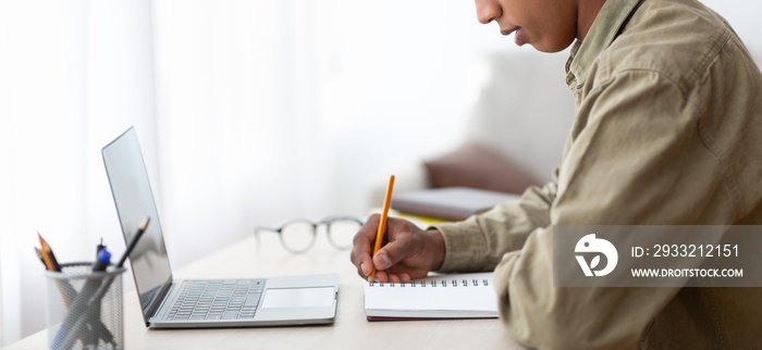 Web-based training. Closeup of black male student writing in copybook near laptop at home, banner de