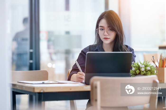 Serious businesswoman sitting at desk in front of laptop, using computer tablet