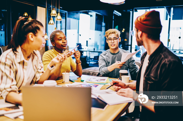 Clever young male and female multiracial hipster students sitting together in coworking space creati