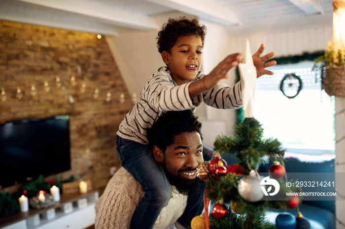 Small black boy decorating Christmas tree with his father and putting star on top.