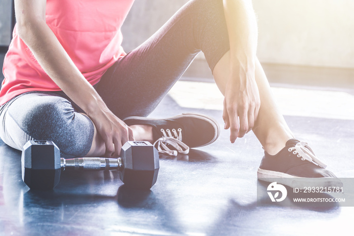 Skinny woman in sportswear sitting on the floor relaxing with the dumbbell lying on the floor. Gym e
