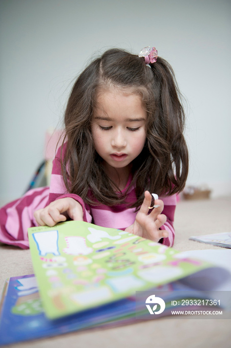 Girl lying on front and reading sticker book