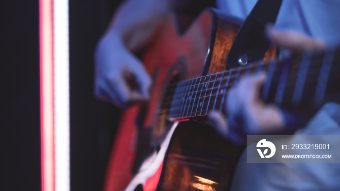 Close up of a guitarist playing an acoustic guitar in a dark room.