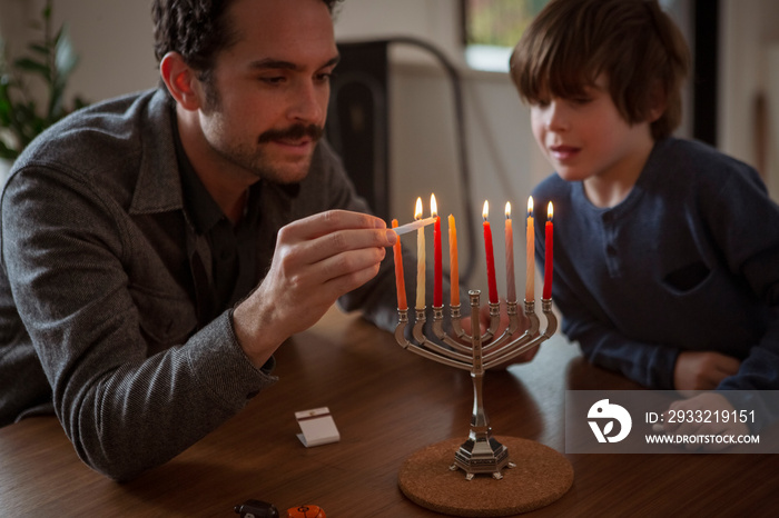 光明节期间，男孩看着父亲在烛台上点燃蜡烛