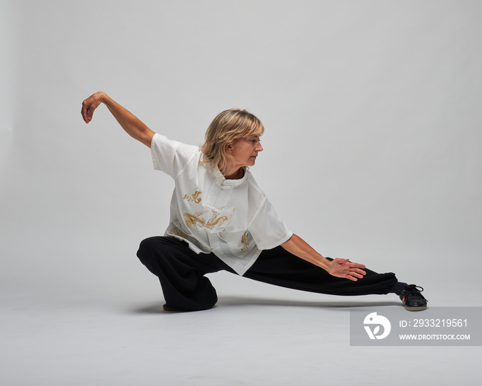 Mature blonde woman practicing Chi kung and Tai Chi on a white background. She wears a traditional w