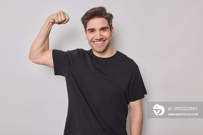 力量概念。积极的英俊男子在健身房训练后展示二头肌，举起肌肉发达的手臂微笑