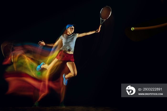 One caucasian woman playing tennis isolated on black background in mixed and stobe light. Fit young 