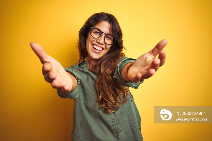Young beautiful woman wearing green shirt and glasses over yelllow isolated background looking at th