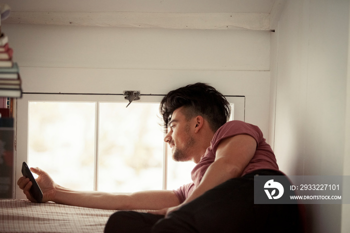 Smiling man using mobile phone while relaxing on alcove window seat at home