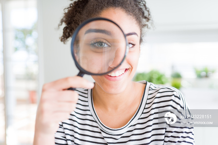 Young african american woman looking through magnifying glass with a happy face standing and smiling