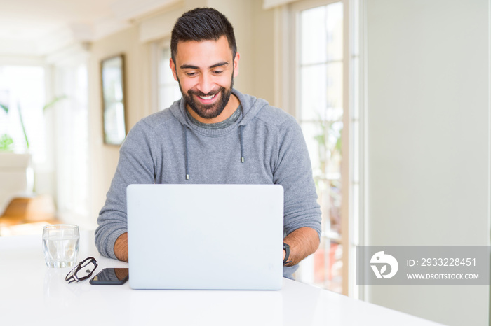 Handsome hispanic man working using computer laptop with a happy face standing and smiling with a co