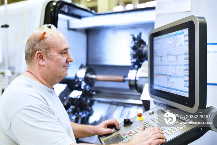 Facharbeiter in der Industrie bedient eine CNC Drehmaschine zur mechanischen Bearbeitung im Maschine