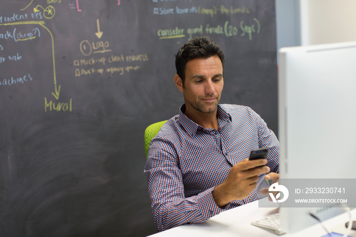 Businessman using smart phone at computer