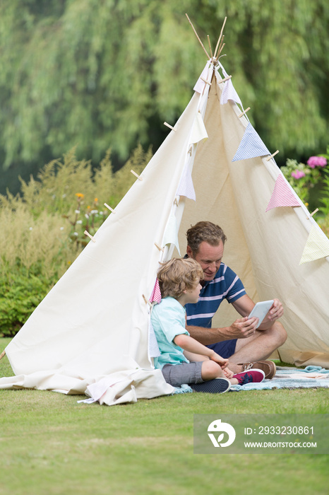 Father and son using digital tablet in teepee in garden