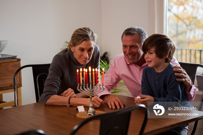 Happy grandparents with grandson looking at menorah on table during Hanukkah