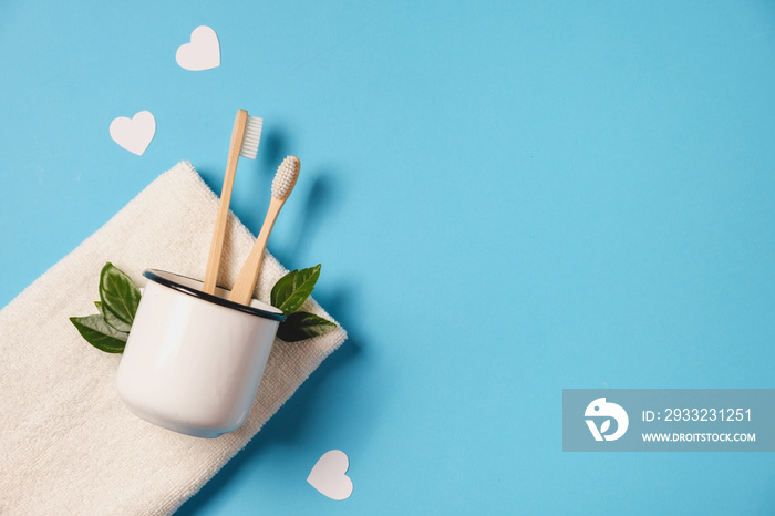 Zero waste concept. Two wooden bamboo eco friendly toothbrushes in metal cup, green leaf, white hear