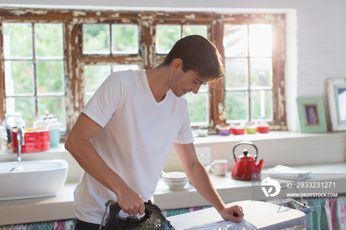 Young man ironing shirt in morning kitchen