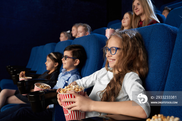 Kids watching movie in cinema, holding popcorn buckets.