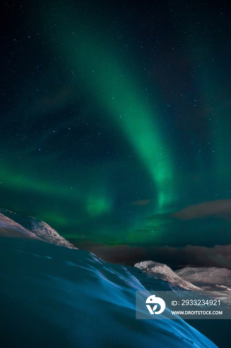 Vertical shot of an aurora in the sky above the hills and mountains covered with snow in Norway