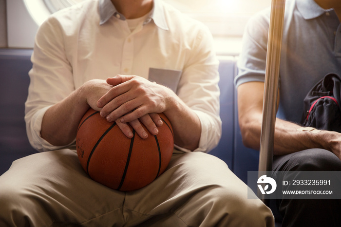 Midsection of man holding basketball while traveling with friend in train