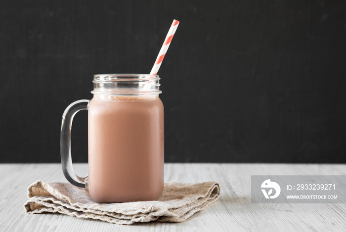 Homemade New England Chocolate Milkshake in a Glass Jar Mug on a white wooden background, side view.