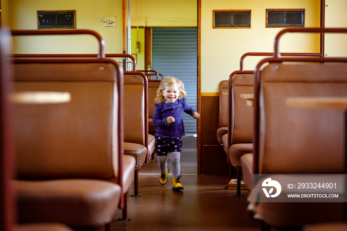 Funny cute little girl running through an empty train waggon. Happy healthy toddler child having fun