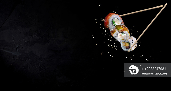 Sushi pieces placed between chopsticks, separated on black background. Traditional japanese food