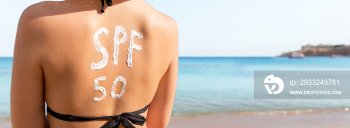 Woman with sunscreen in form of SPF 50 word on her back sunbathing at the beach. Sun protection fact