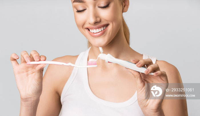 Girl Applying Toothpaste On Tooth Brush Over Gray Studio Background.