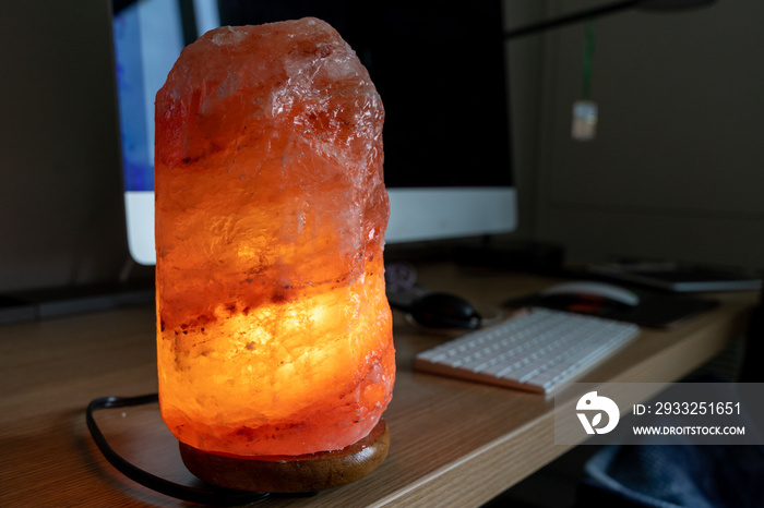 一盏橙粉色发光的喜马拉雅盐灯放在电脑桌上。工作中的平静概念