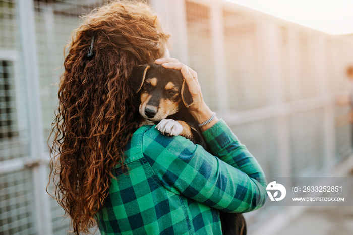 Young adult woman holding adorable dog in animal shelter.