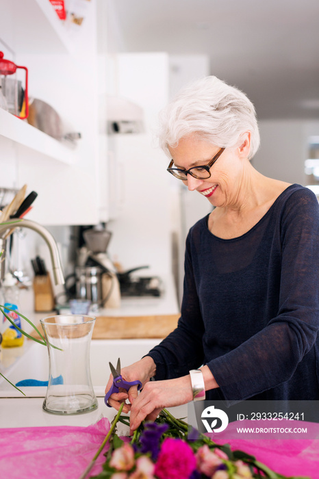 Senior woman arranging bouquet in kitchen