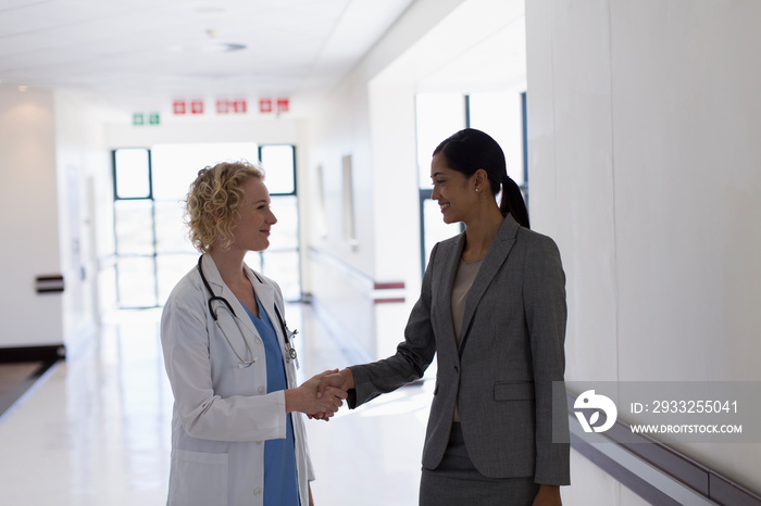 Female doctor and administrator shaking hands in hospital corridor