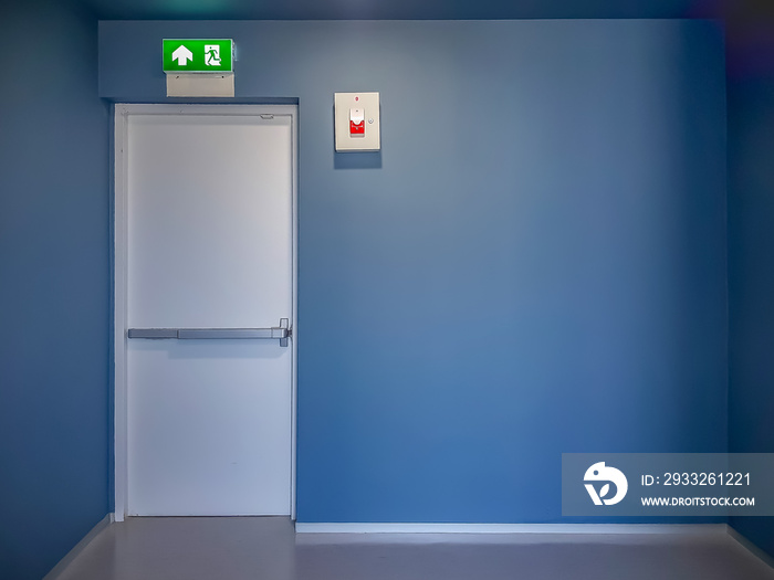 Fire exit door and emergency red light alarm box on blue wall in modern style building.